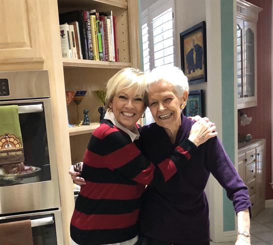 Two smiling women share a warm embrace in a cozy kitchen filled with family memories.