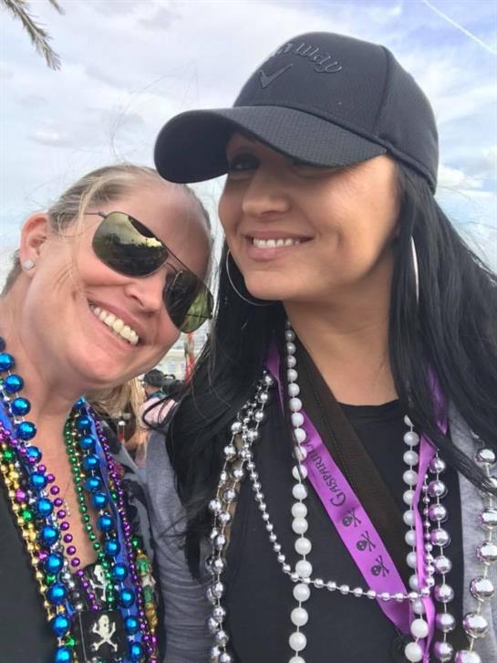 Women smiling at an outdoor festival, wearing festive beads and enjoying the celebration.