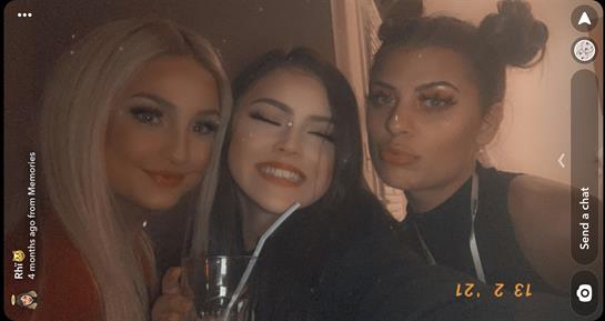 Three friends celebrate together, sharing smiles and drinks in a lively atmosphere at night.