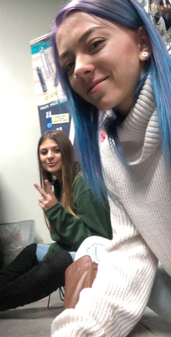 Two girls smile while sitting in a relaxed indoor environment, showcasing their friendship.