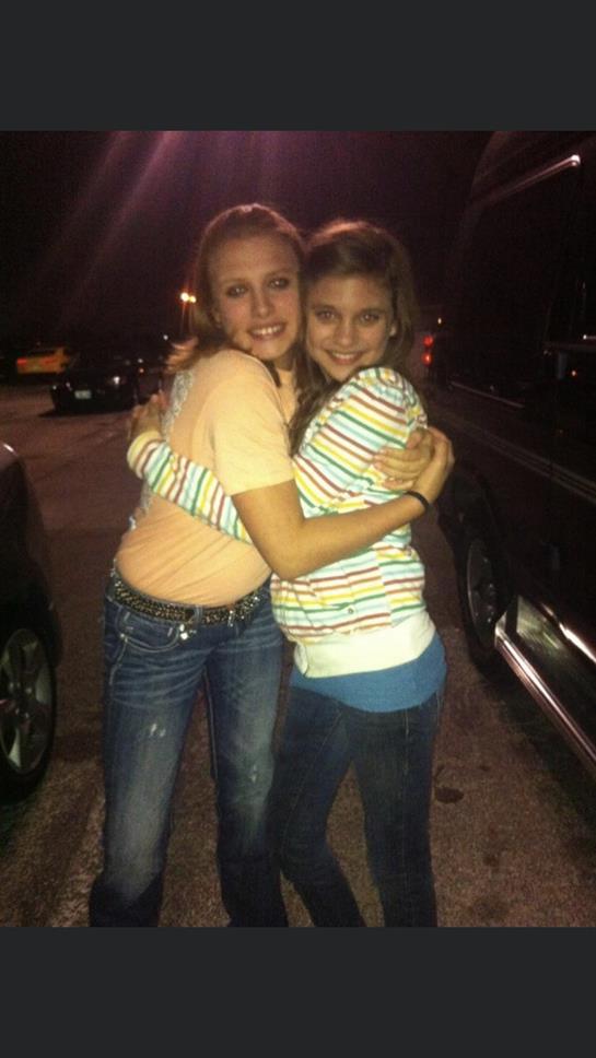 Friends share a warm hug in a lively parking lot on a cool evening, illuminated by streetlights.