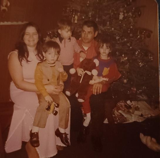 Kids sit with adults by a Christmas tree, capturing a joyful holiday atmosphere and family love.
