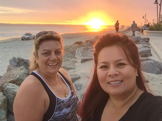 Two women smile as they enjoy a vibrant sunset on the beach with others in the background.