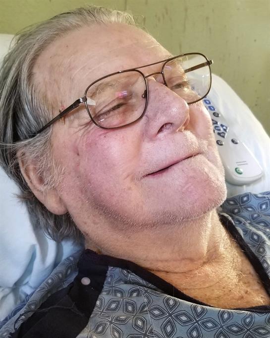 An elderly man lies in a hospital bed, displaying a calm expression as he relaxes in recovery.