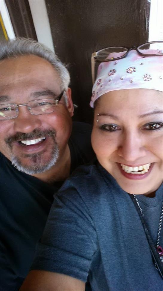 A couple smiles joyfully at the camera in a cozy indoor setting.