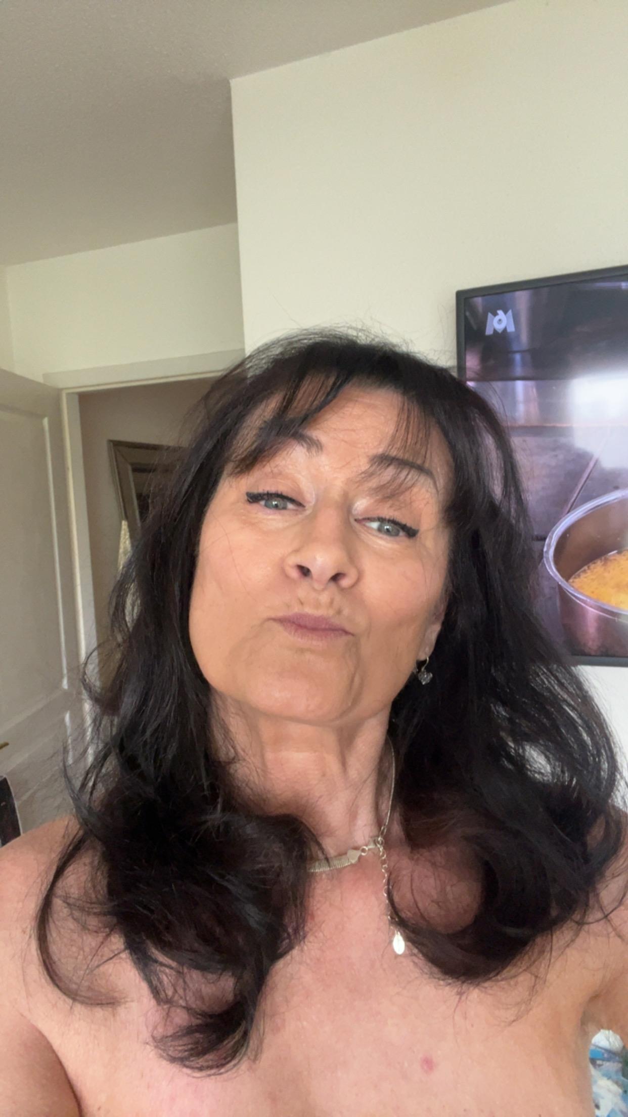 Woman with dark hair smiles at the camera in a bright, cozy indoor setting.