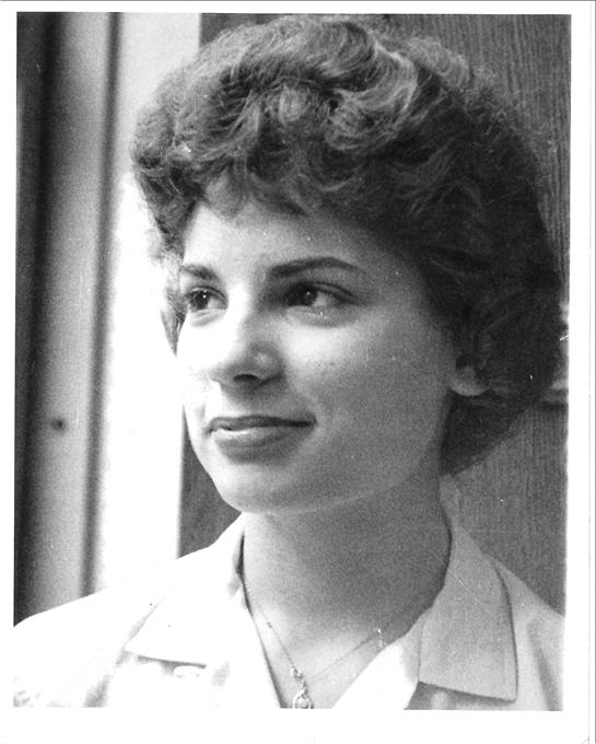 A portrait of a young woman with curly hair, smiling softly against a light background.
