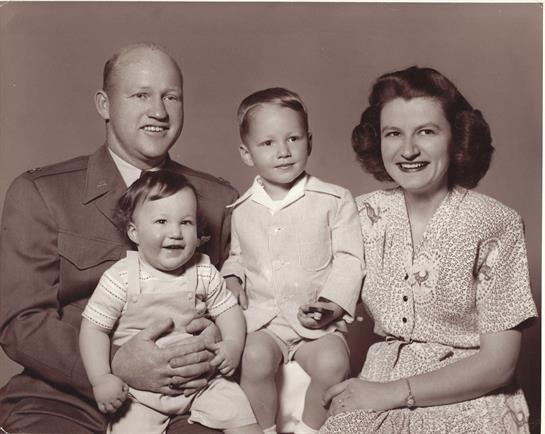 Parents pose with their two young children in a vintage studio setting, showcasing family bonds.