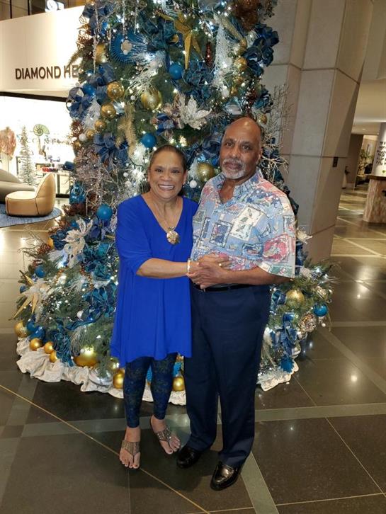 Couple smiling for a picture beside a beautifully decorated Christmas tree in a hotel lobby.