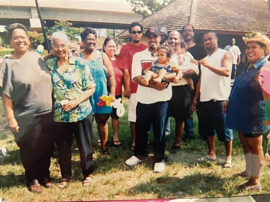 A joyful family assemble in a park, with multiple generations smiling and engaging with each other.