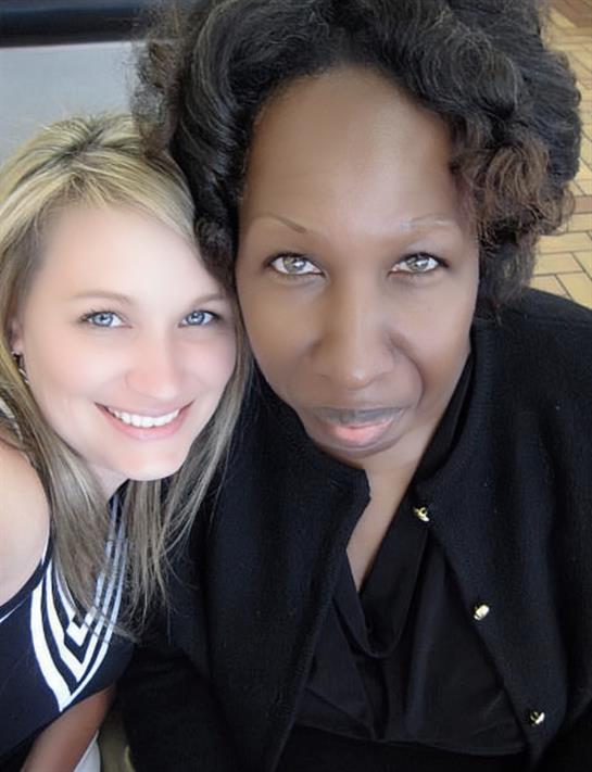 Two women are enjoying a lighthearted moment, smiling while posing closely together.