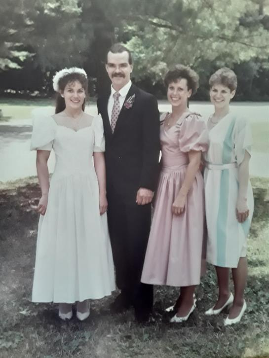 Group of four friends smiling together at a wedding, wearing elegant attire in a garden setting.