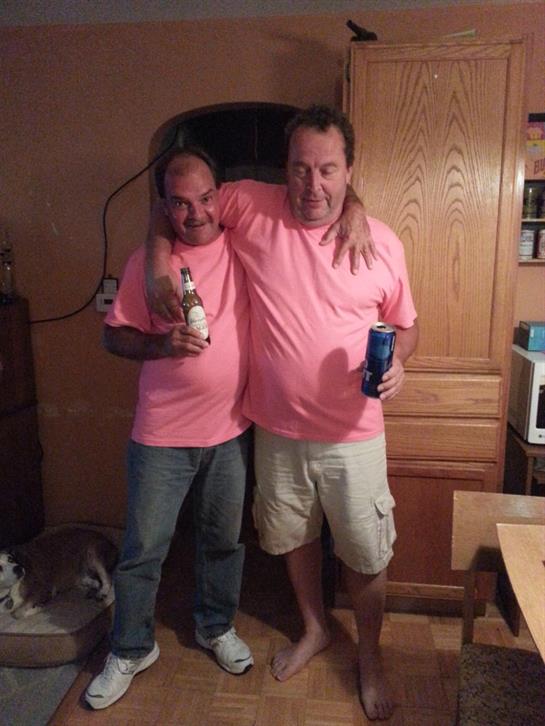 Two friends happily embrace with drinks in a lively home during a casual get-together.