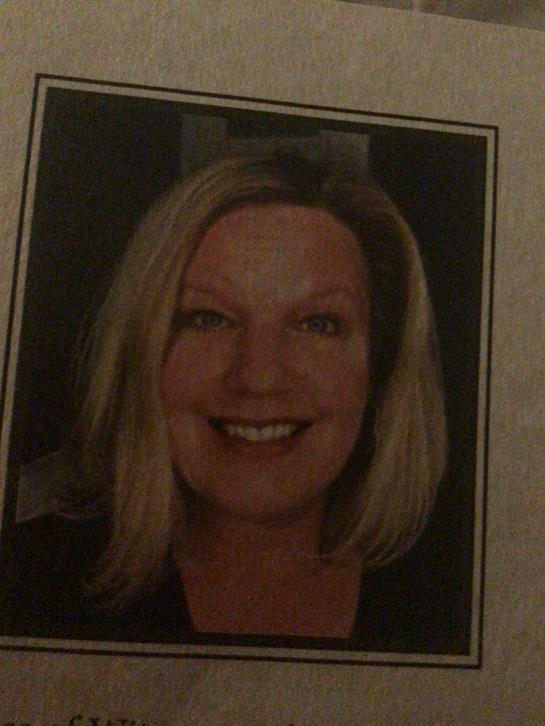 A woman with blonde hair smiling warmly while enjoying a bright indoor atmosphere.