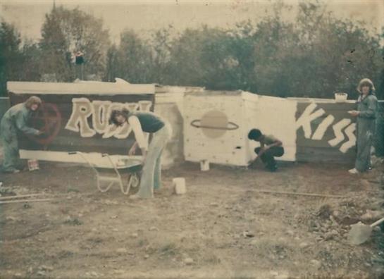 Two individuals are actively painting a mural on an outdoor wall, showcasing colorful designs.