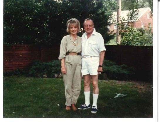 Two people pose happily in a lush garden, enjoying a sunny afternoon outdoors.