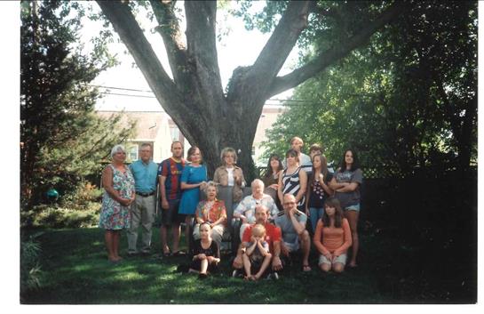 A diverse group of family members poses together outdoors, enjoying a sunny day in the yard.