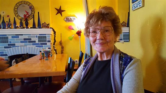 Elderly woman enjoys a cheerful moment in her cozy home dining space filled with decor.