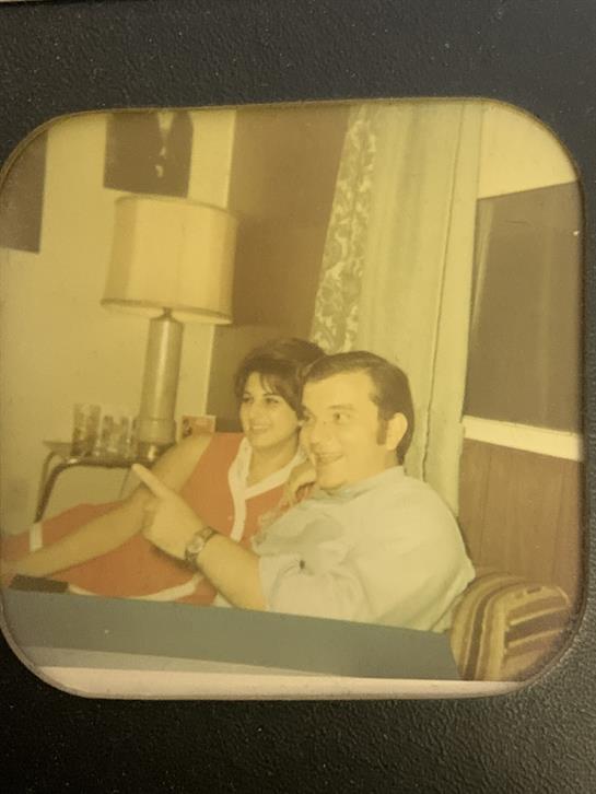 A couple sits closely on a sofa, chatting and laughing in a cozy living room.
