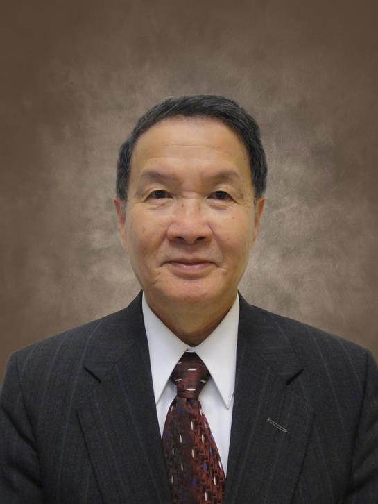 A well-dressed man smiles confidently while standing in front of a simple backdrop.