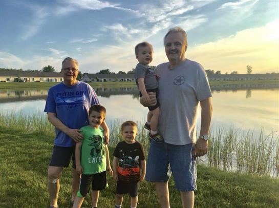 Four family members smile and pose near the water's edge on a sunny afternoon.