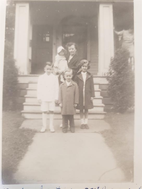 Four children and one adult pose together on the steps of a house, showcasing vintage attire.