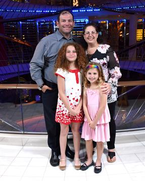 A family stands together, smiling joyfully against a vibrant background on a cruise ship.