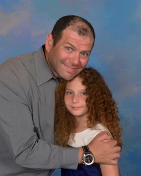 A man and a girl share a warm embrace in a photo studio, smiling happily at the camera.