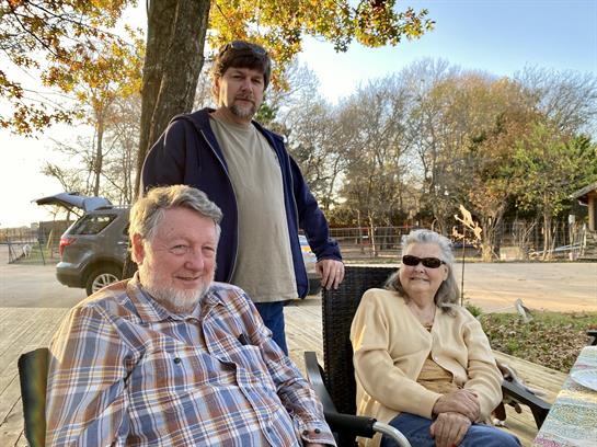 Three friends sit together outdoors, enjoying a sunny afternoon with smiles and conversation.