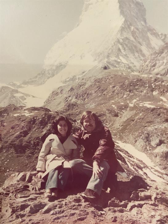 Two friends relax on a rocky outcrop, surrounded by stunning mountain views on a sunny day.