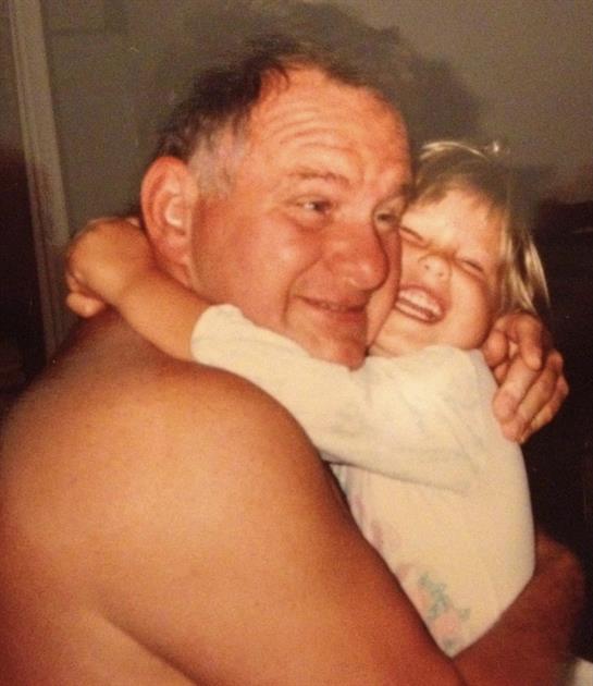 A grandfather hugs his smiling granddaughter in a warm, loving moment.