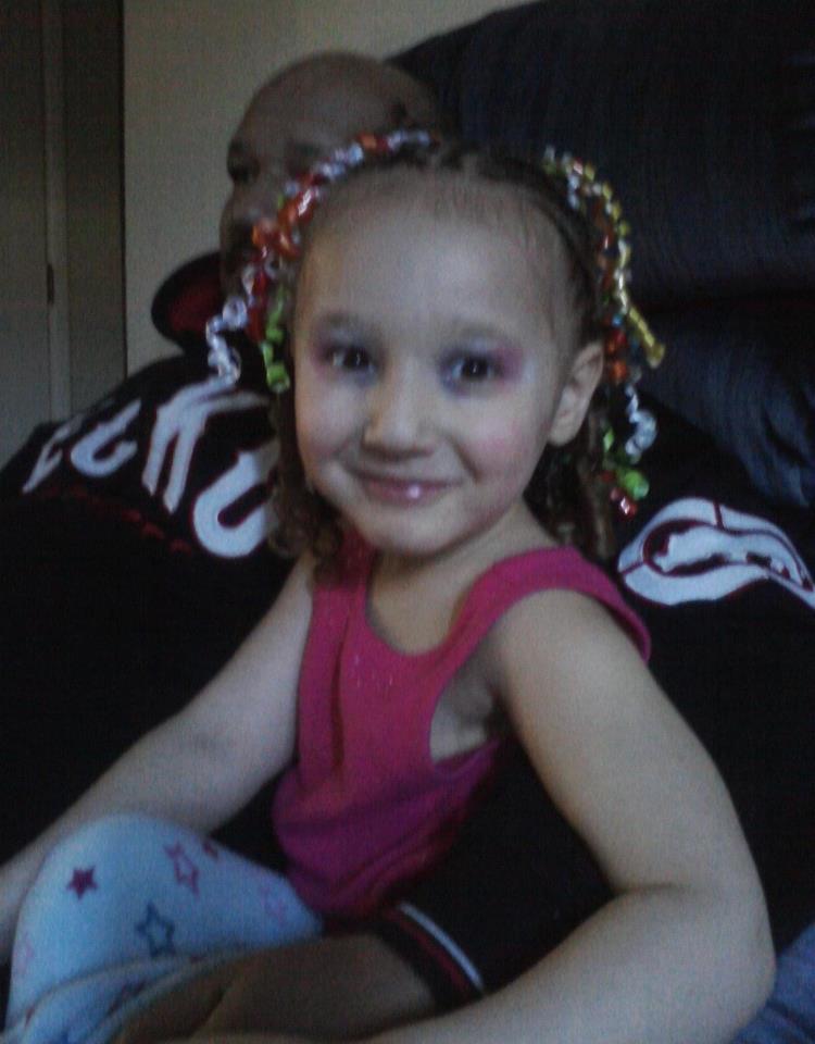 A cheerful girl with a vibrant hairstyle and playful makeup sits comfortably on a couch.