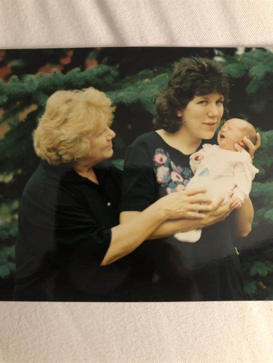 A mother and grandmother share affection while cradling a newborn in a serene garden setting.