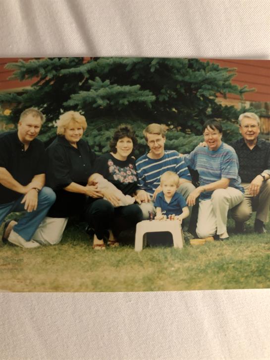 Group of adults and children enjoying a family gathering in a grassy area beside a large tree.