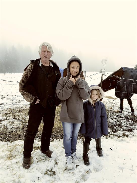 Two children and an adult stand in the snow, smiling with a horse nearby on a foggy day.