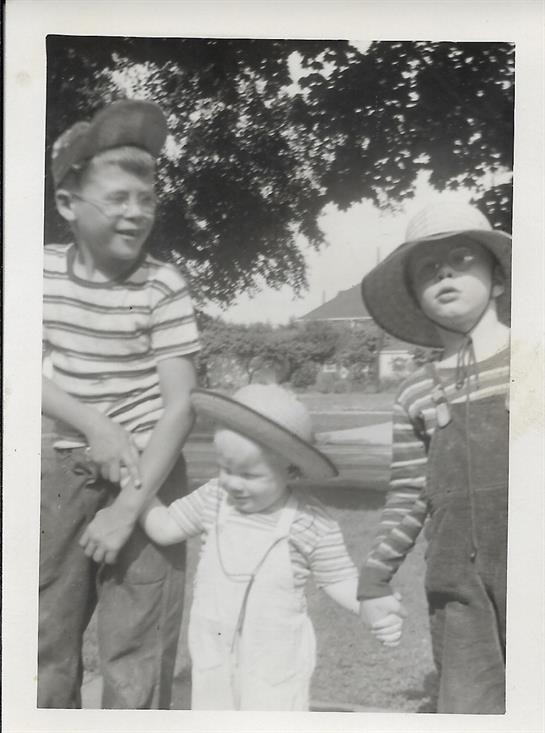 Three kids enjoy a playful moment outside, holding hands and smiling under the sun.