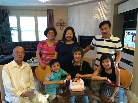 Family members enjoy a joyful birthday celebration around a table with a cake in a warm living room.