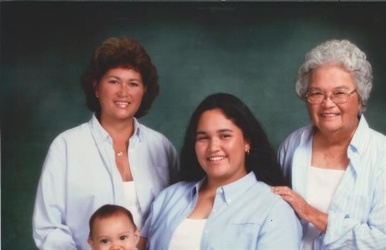 Four family members, including a baby, pose together in a bright indoor studio smiling happily.