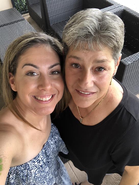 Two women pose closely together, enjoying a relaxed moment outdoors with smiles.