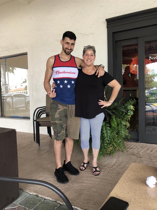 A young man wearing a tank top and shorts stands next to a smiling woman in casual clothes.