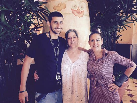 Three family members stand together, sharing smiles in a lush, tropical setting.