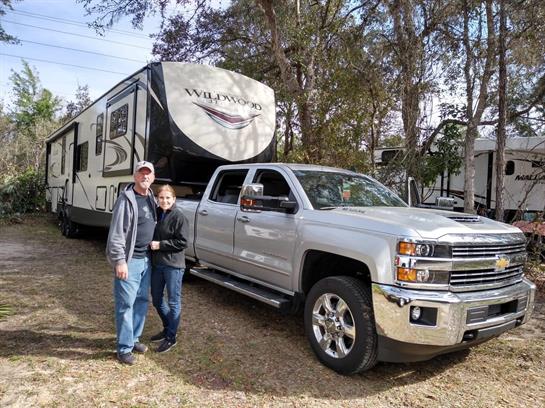 A family stands beside their truck and RV, enjoying a relaxing day in nature at a campsite.