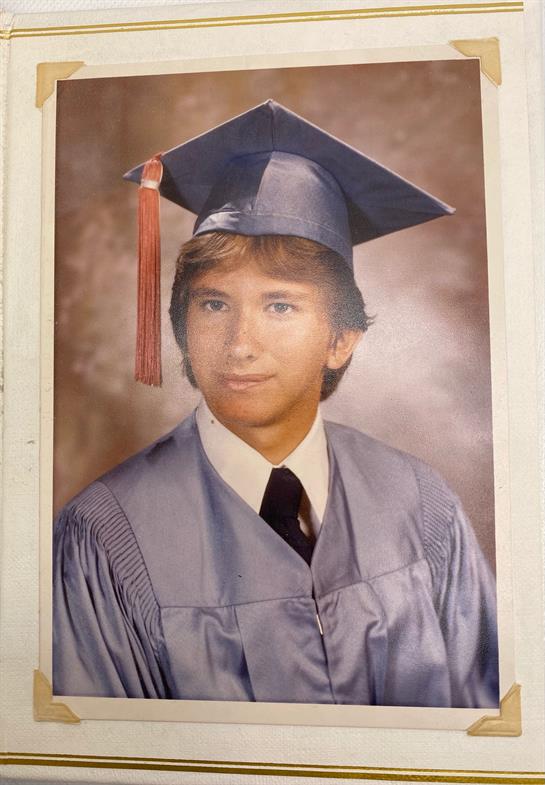 A young man poses in graduation attire with a confident smile, capturing a moment of achievement.