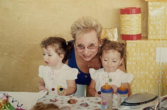 Grandmother joyfully poses with her twin granddaughters at a festive gathering in a warm space.