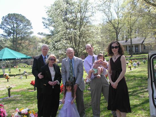 Relatives gather in a peaceful cemetery, honoring shared memories under blooming trees.