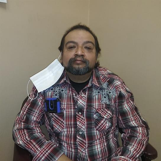 Person sits calmly in a medical office, wearing a mask and casual plaid shirt while waiting.