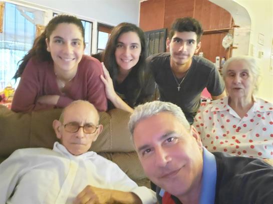 Six family members smile together in a cozy living room for a group photo.