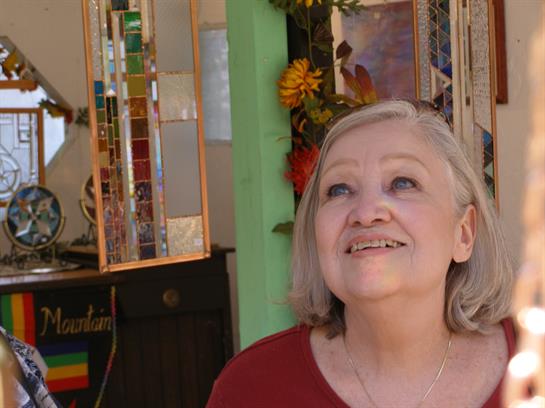 Elderly woman with silver hair smiles brightly while exploring colorful decorations in a local shop.