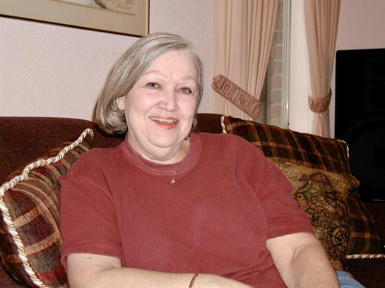 An older woman enjoys a moment of relaxation on a couch filled with decorative pillows.