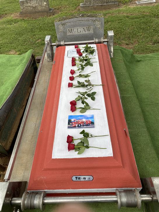 Red roses and a cherished photo decorate a coffin at a burial location in nature.
